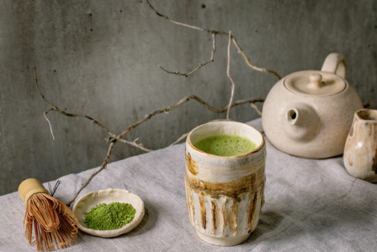 Traditional japanese hot green frothy tea matcha in handmade ceramic cup, powdered matcha, teapot and bamboo whisk standing on grey linen tablecloth, Healthy drink