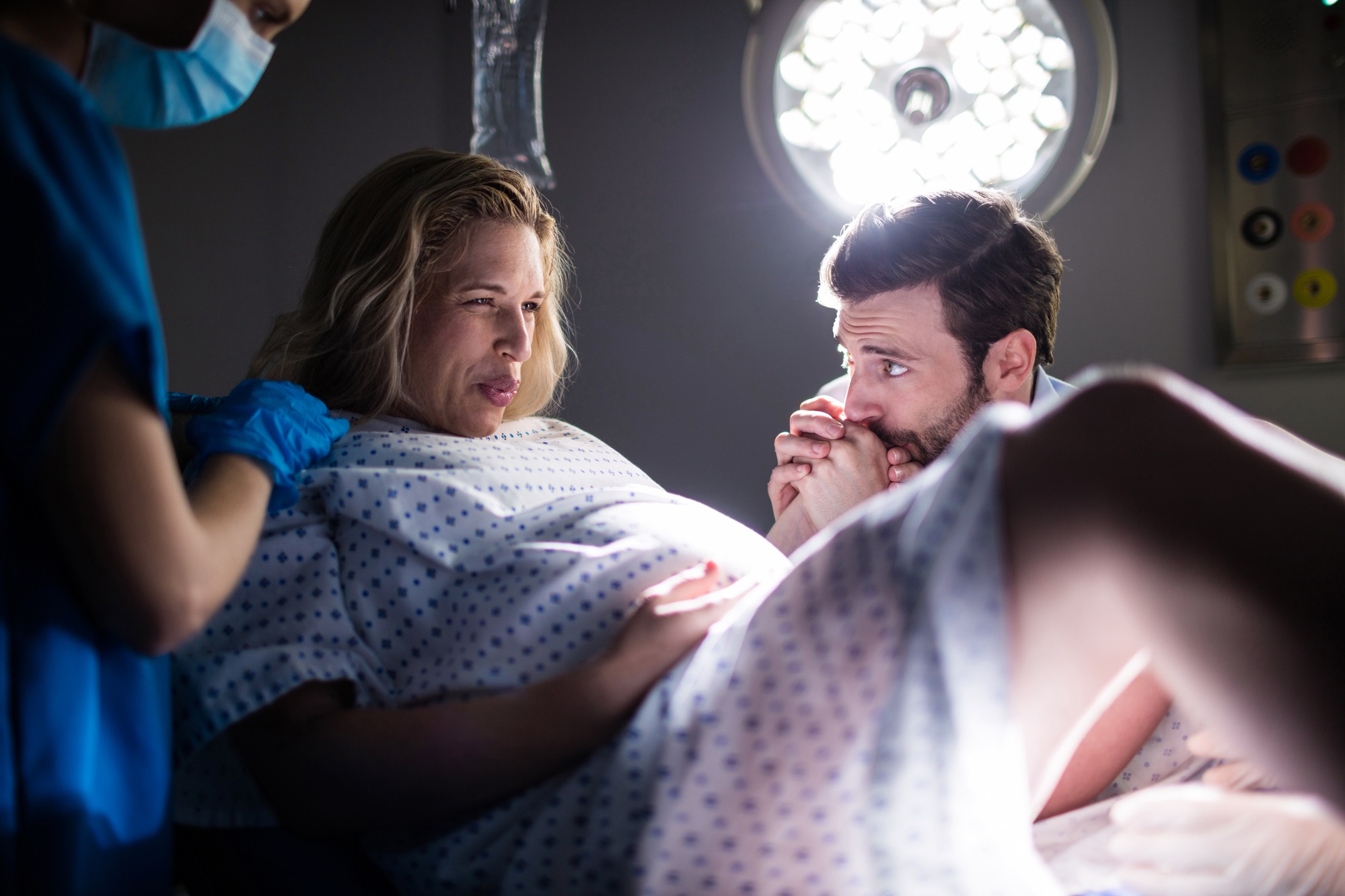Doctor examining pregnant woman during delivery while man holding her hand in operating room
